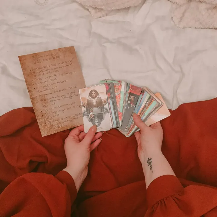 Hands holding a tarot deck above a notebook