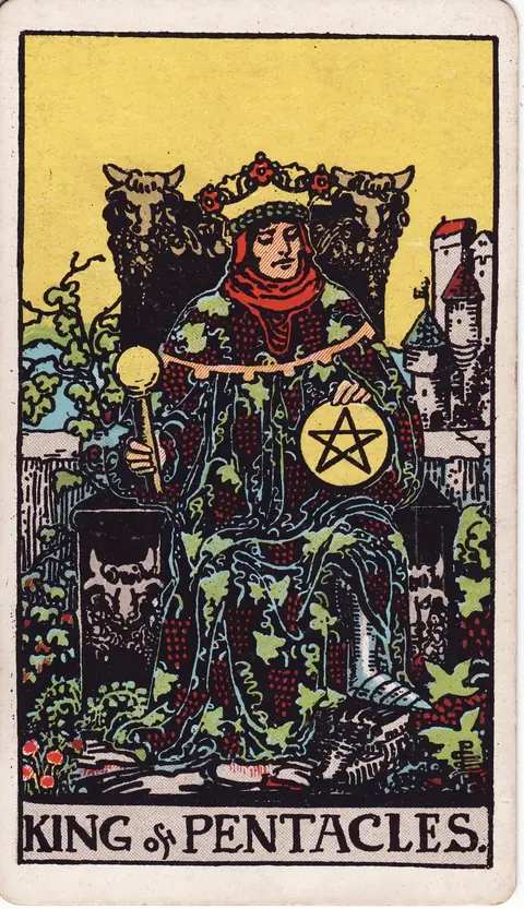A king holding a sceptre and pentacle on a bull-decorated throne among vines with a castle behind him