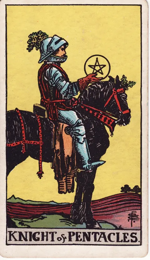 An armoured knight on a dark horse holding a gold pentacle before cultivated fields