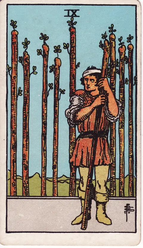 A bandaged man gripping a wand with eight upright staffs forming a barrier behind him