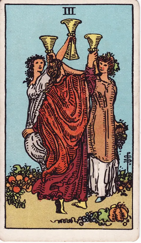 Three women raise golden cups as they dance together among flowers and harvest produce beneath a clear sky.