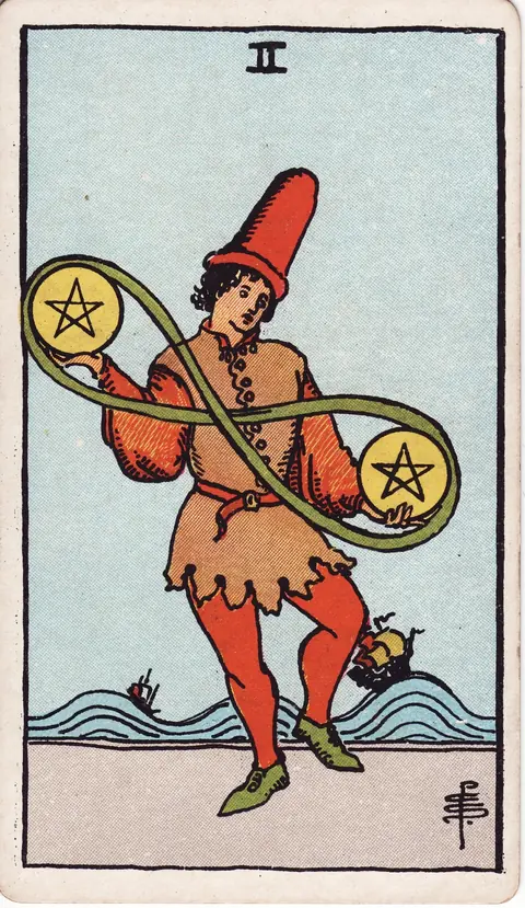 A young man juggles two pentacles joined by an infinity-shaped band while two ships ride high waves behind him.