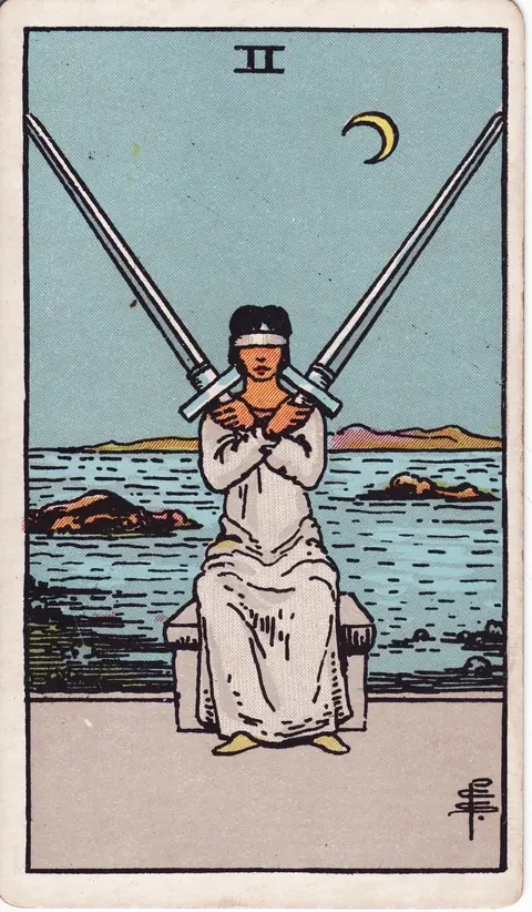 A blindfolded woman sits before the sea, holding two crossed swords beneath a crescent moon.