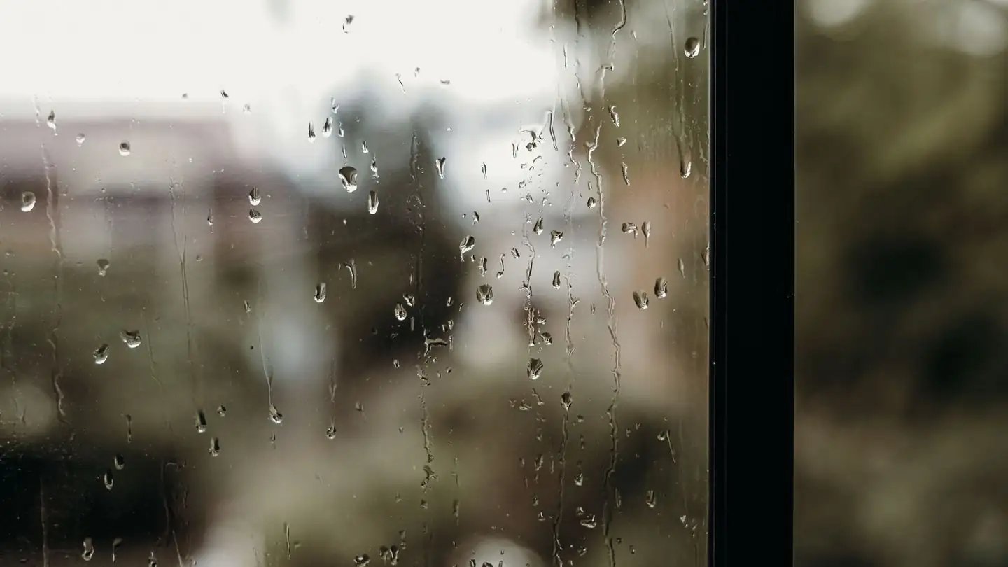 Raindrops cover a window with a blurred view beyond.