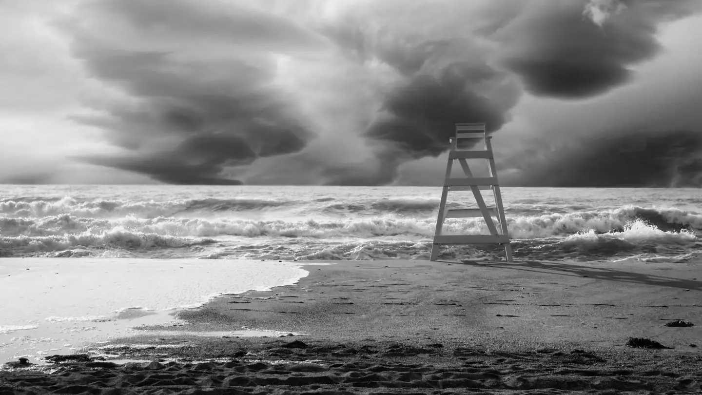 A lifeguard tower stands on a beach beneath storm clouds.