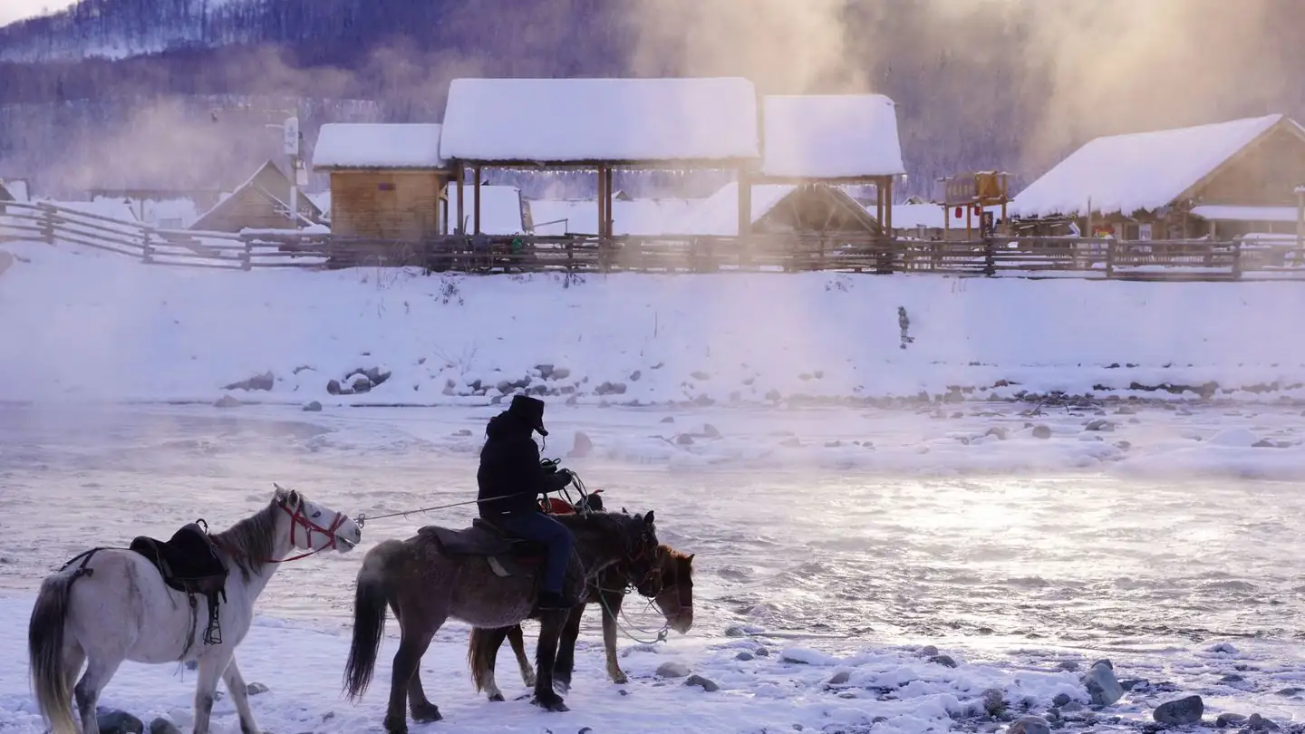 A rider on horseback travels beside a snowy river.