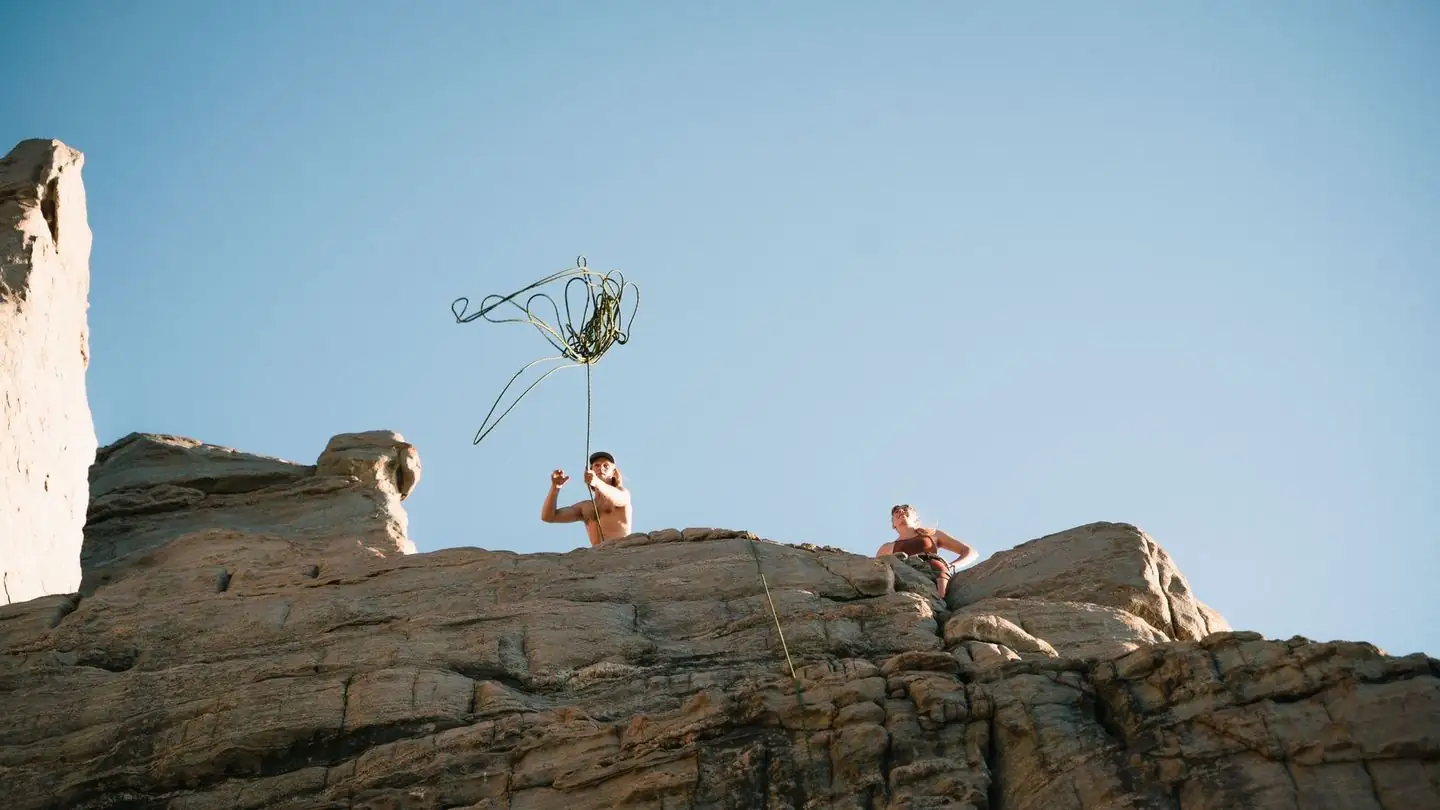 Two climbers work their way up a sunlit cliff.