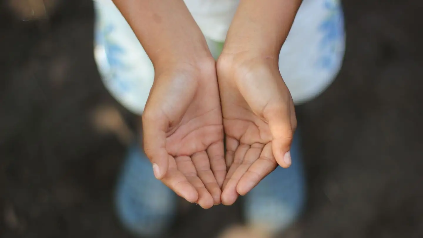 A child holds both hands open, palms facing upward.