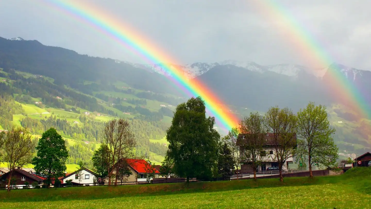 A rainbow arches over a village beneath mountains.