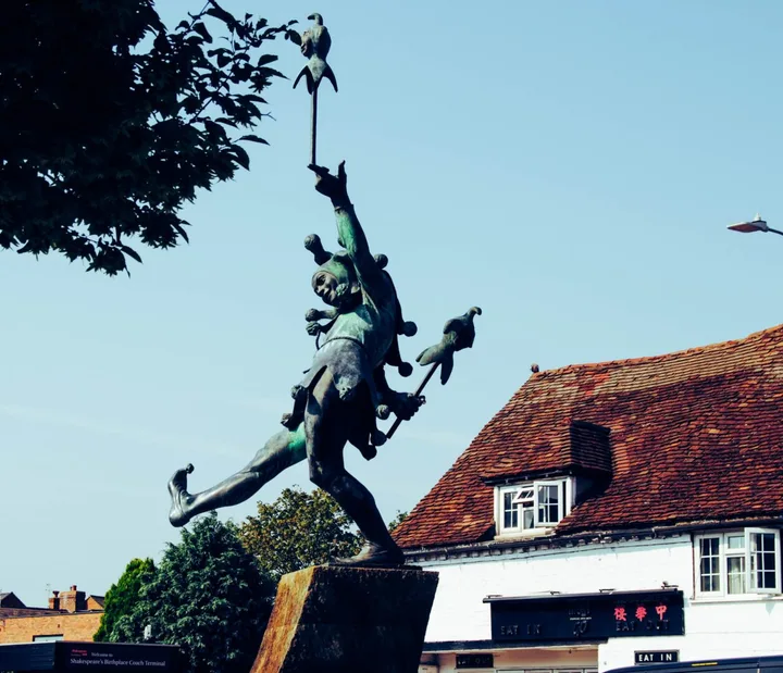 A bronze jester sculpture balancing in front of a building