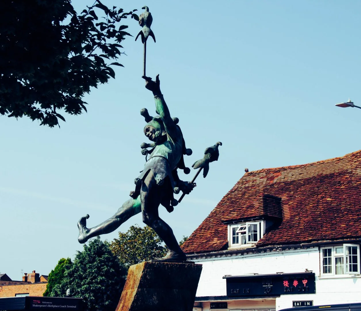 A bronze jester sculpture balancing in front of a building