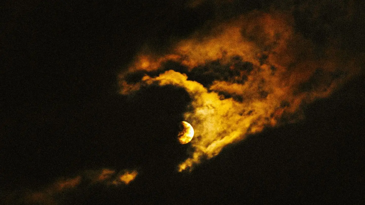 The moon shining through clouds in a dark night sky
