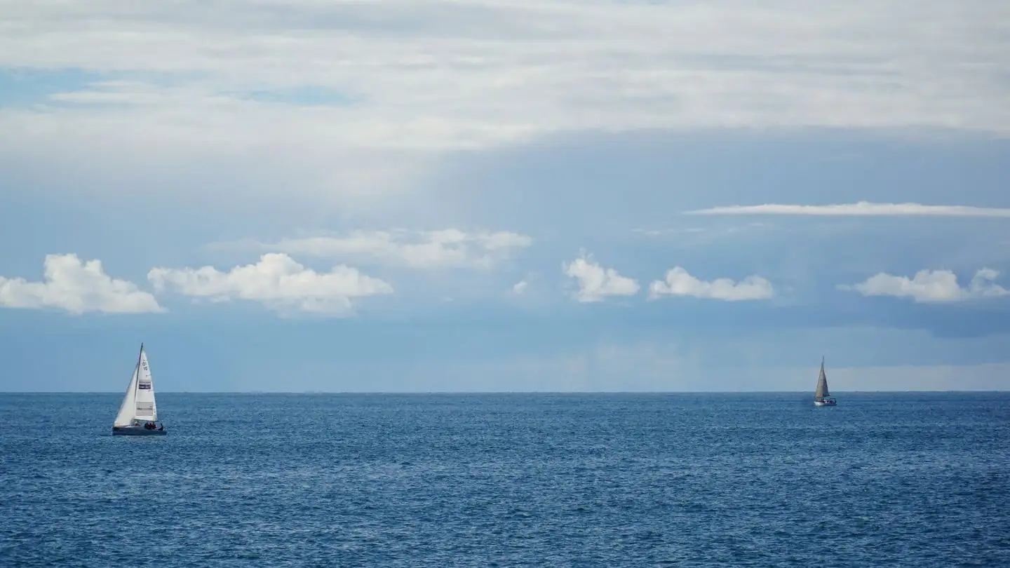 Two sailboats cross the sea beneath a cloudy sky.