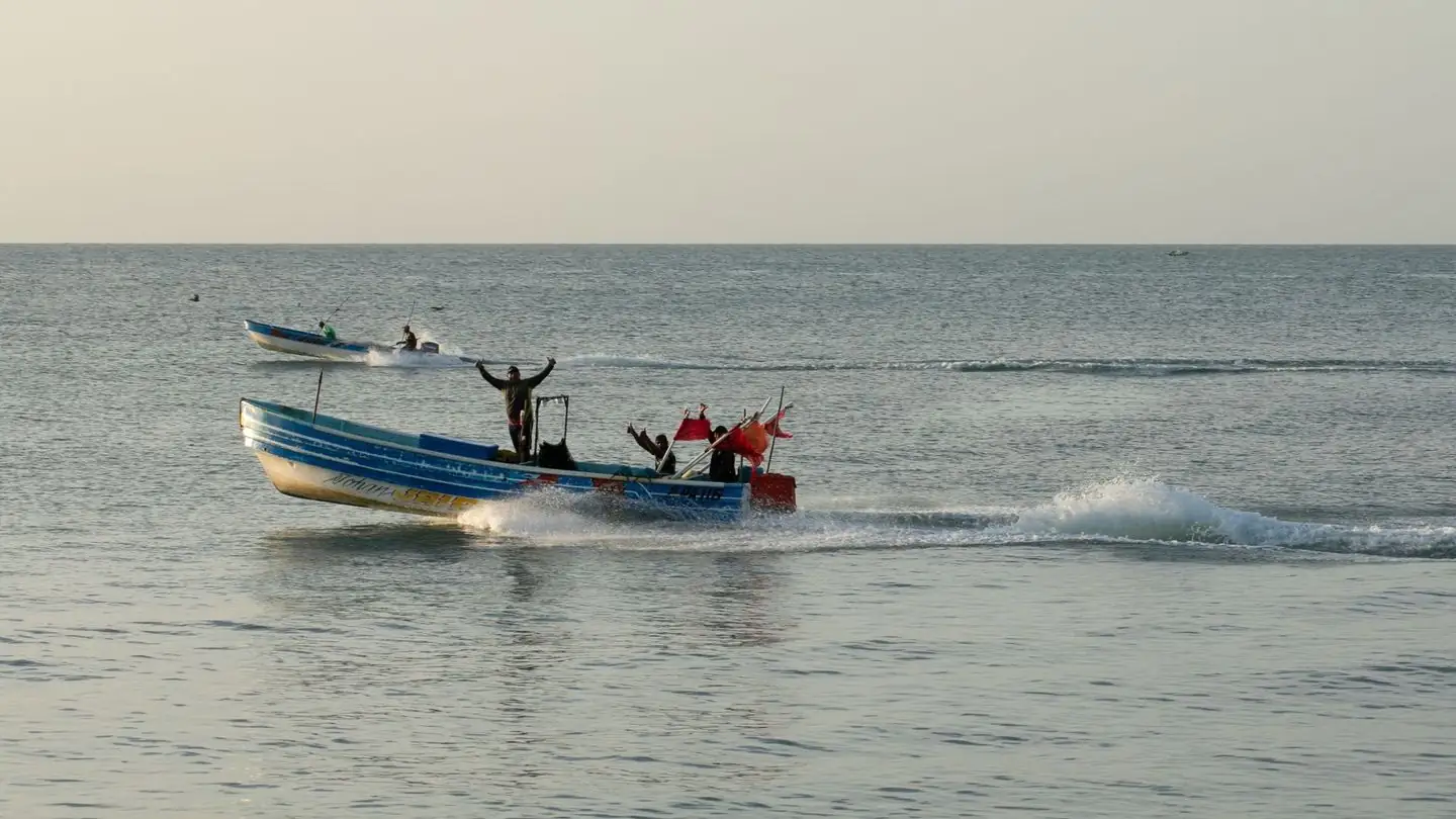 A man waves from a motorboat crossing the sea.